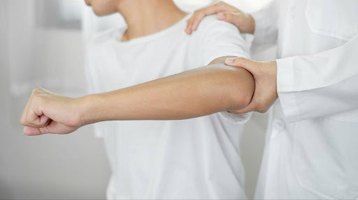 A young man conducting elbow stretches with the help of a doctor.